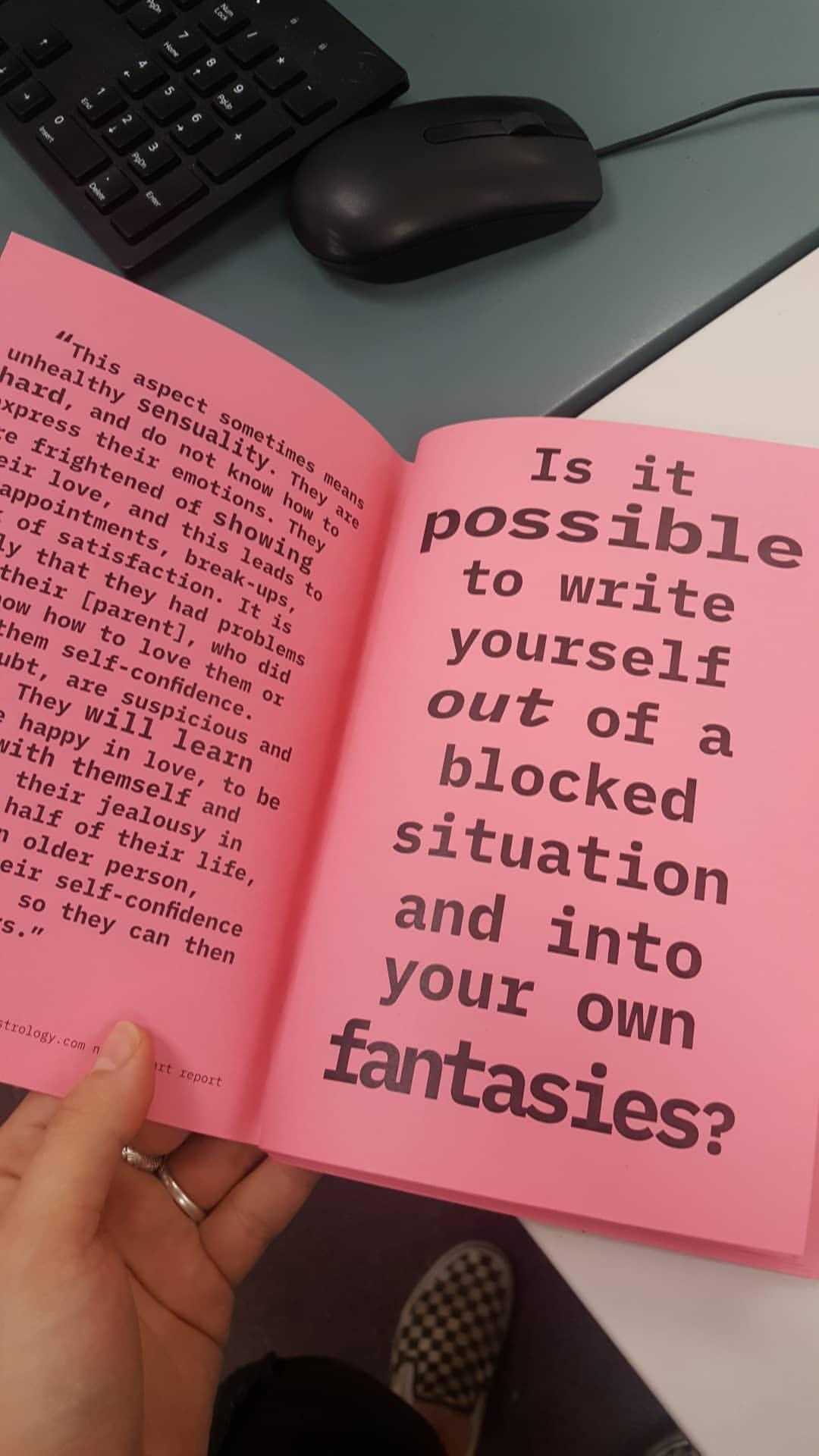 A zine printed on pink paper is open to a page that says 'is it possible to write yourself out of a blocked situation and into your own fantasies?'