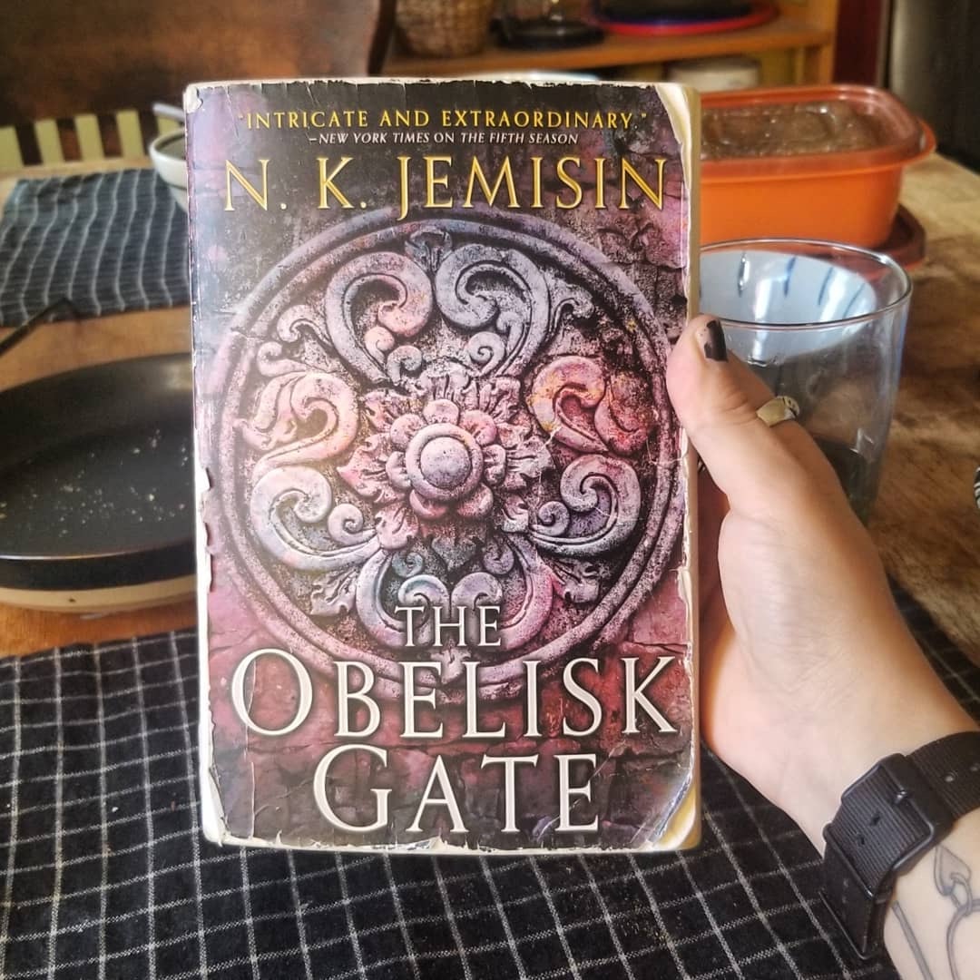 me holding up the Obelisk Gate book over my kitchen table